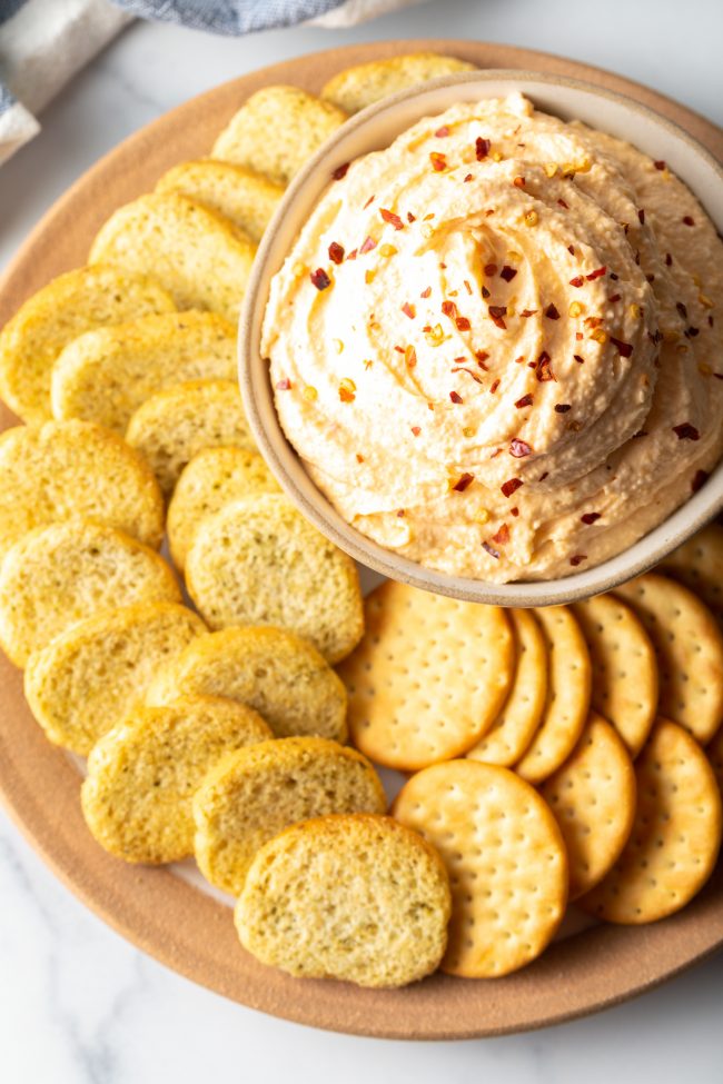 top view bowl of cheese spread with crushed red pepper on top, surrounded by slices of crunchy bread and crackers