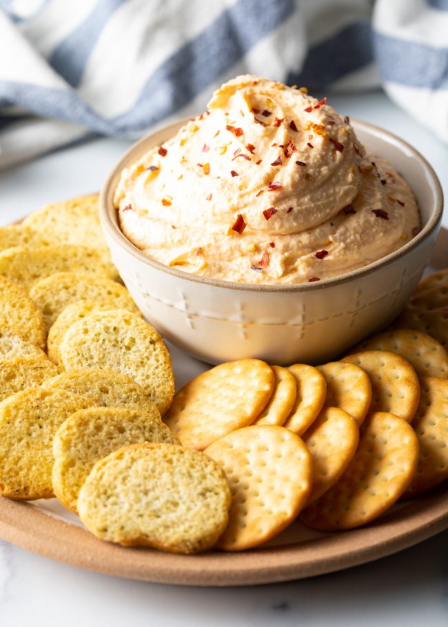 bowl of smoked cheese and sour cream dip on a plate surrounded by crackers and toasted bread slices