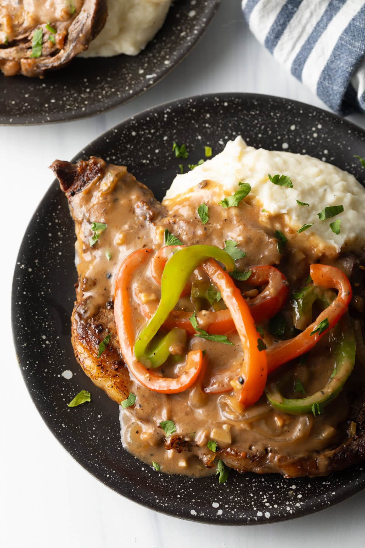 top view mashed potatoes smothered with steak and gravy and peppers on a black plate