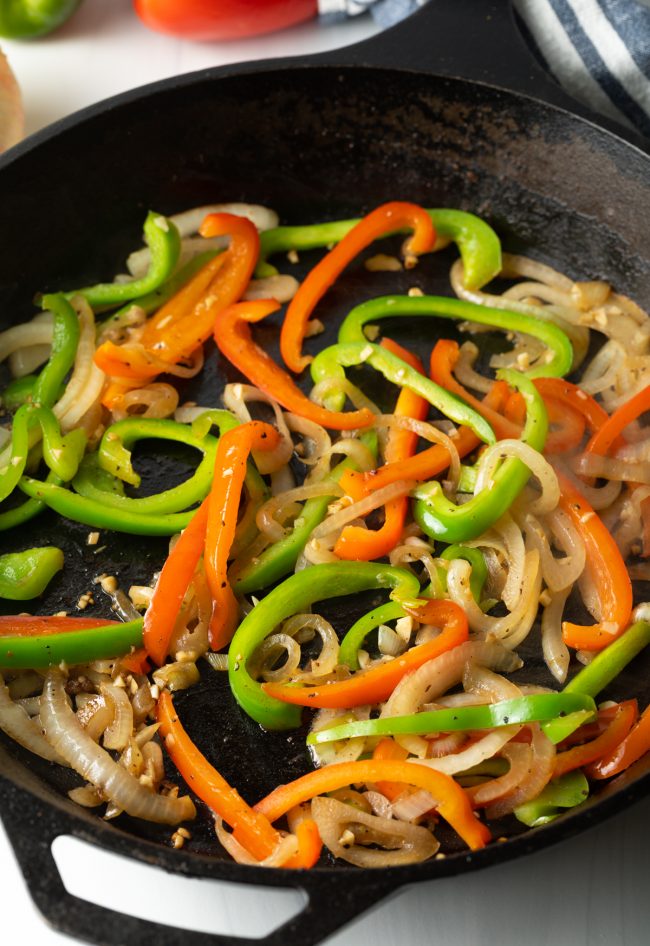 sliced bell peppers and onions in a cast iron skillet pan