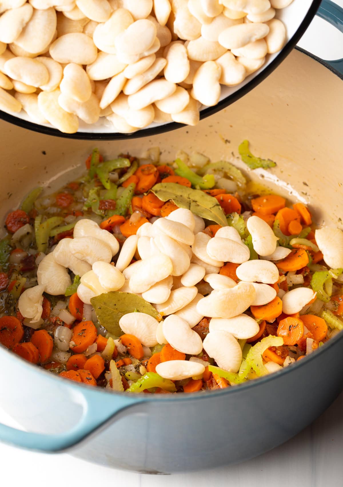 Adding soaked lima beans to the pot with the trinity