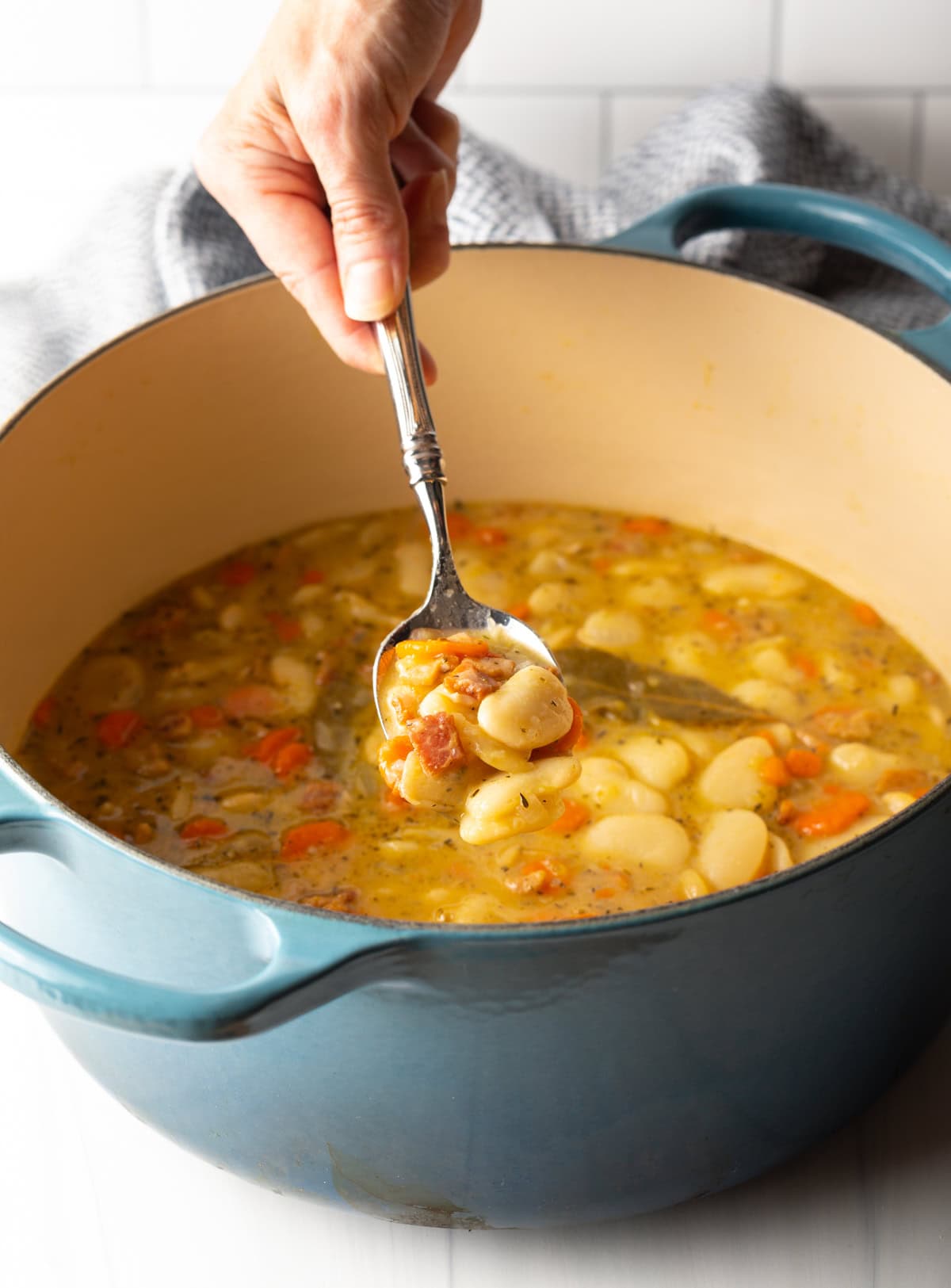 hand spooning butter beans with bacon from a large pot