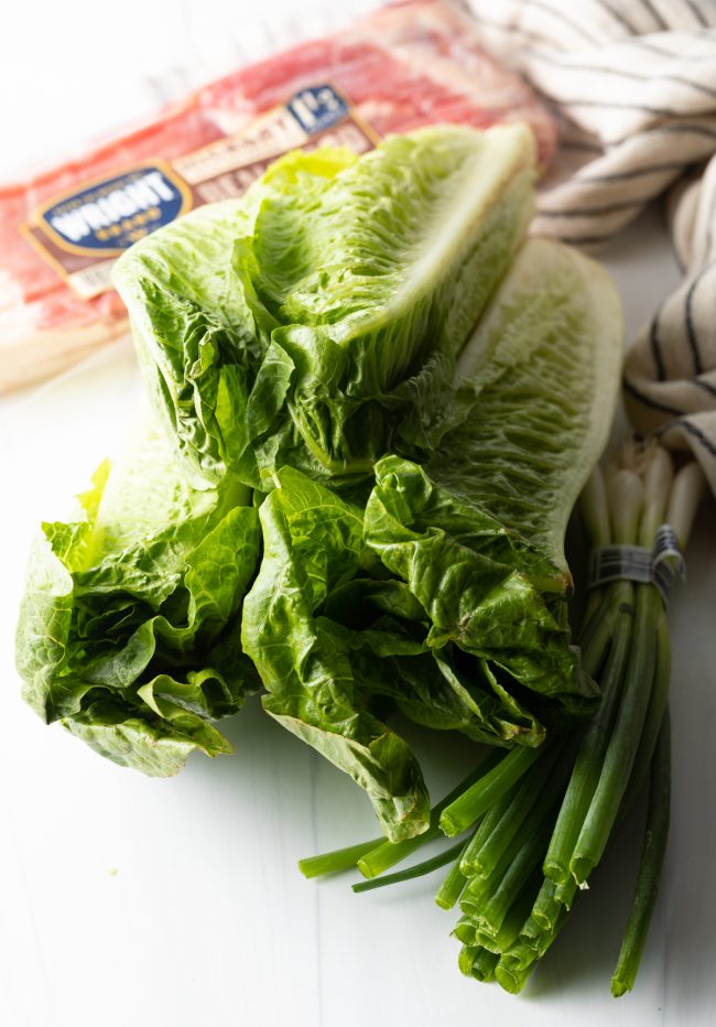 bundles of romaine, scallions, and bacon in the background all on a white background