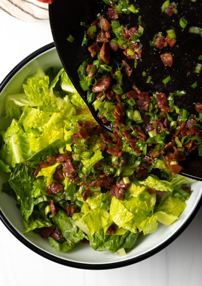 pouring the hot bacon and grease with scallions into the bowl with chopped romaine