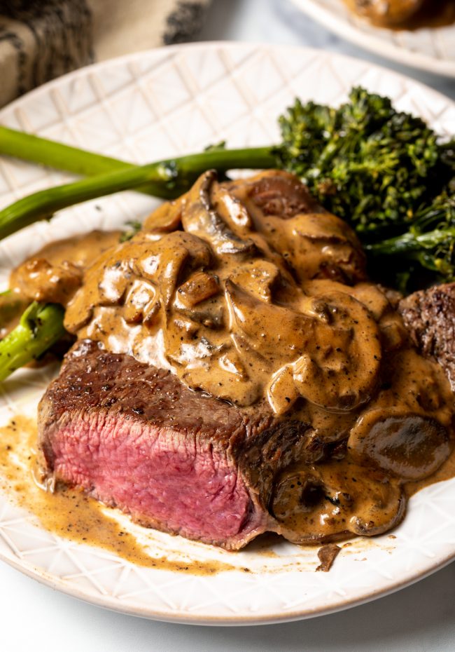 view of sliced steak on a white plate, topped with mushroom cream sauce