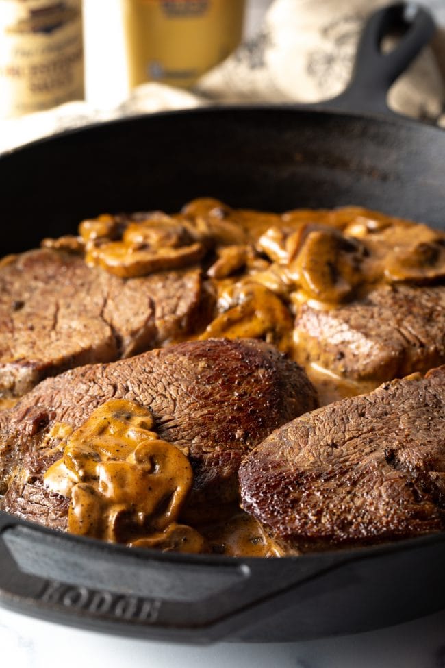 4 steaks sitting in a mushroom cream gravy in a cast iron skillet.