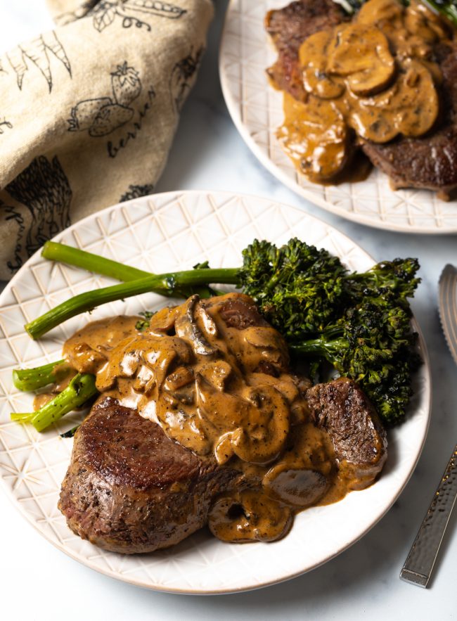 top view two white plates with copycat Cheesecake Factory steak Diane and broccolini
