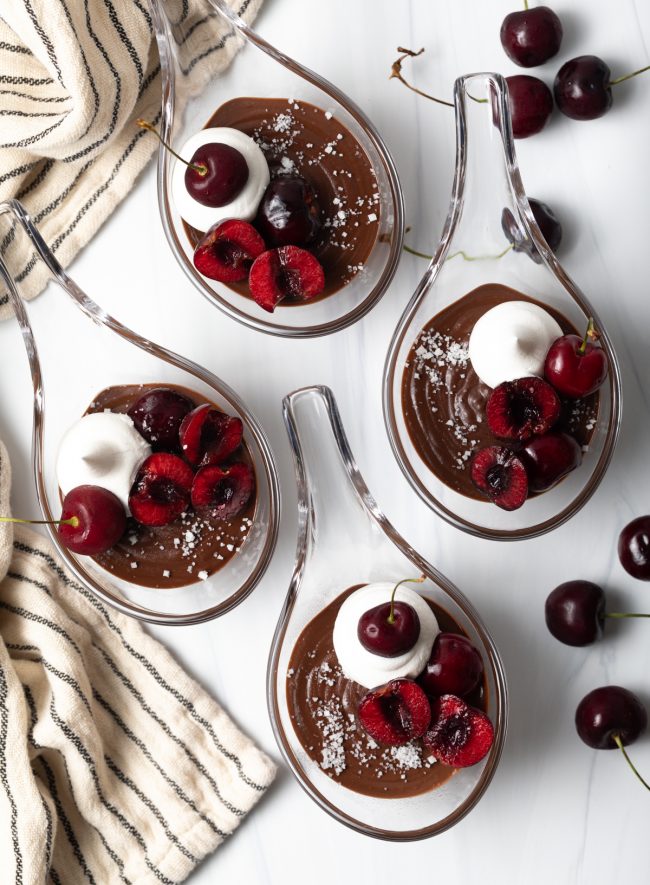 top view four servings of Italian chocolate puddings with cherries, whipped cream, and sea salt
