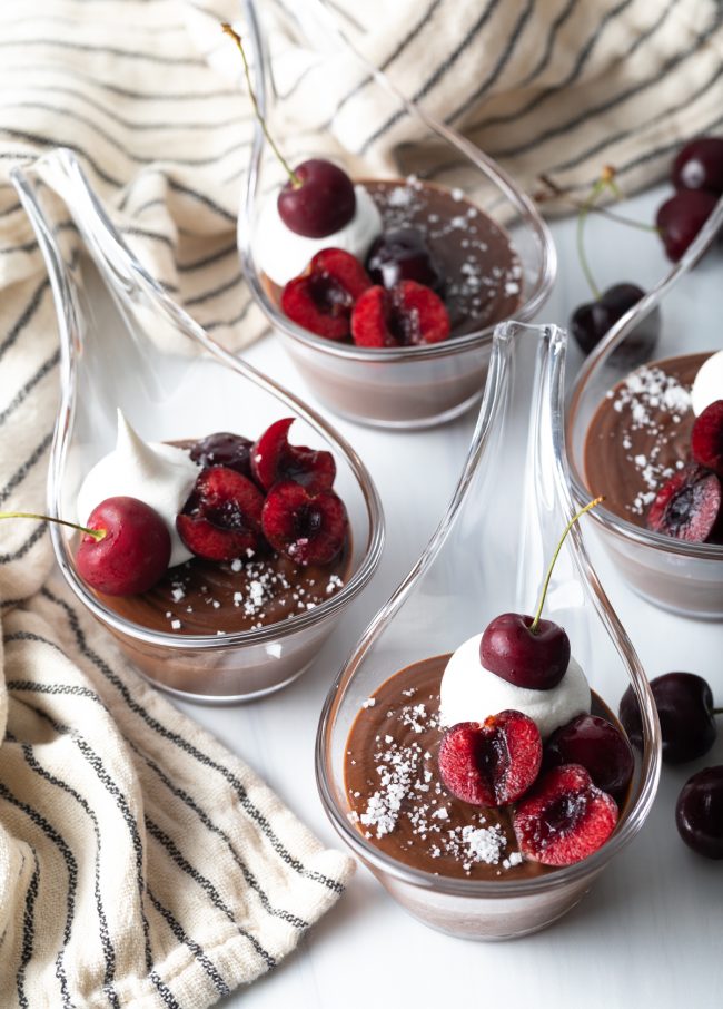four individual servings of chocolate Italian pudding with fresh whipped cream, cherries, and sea salt