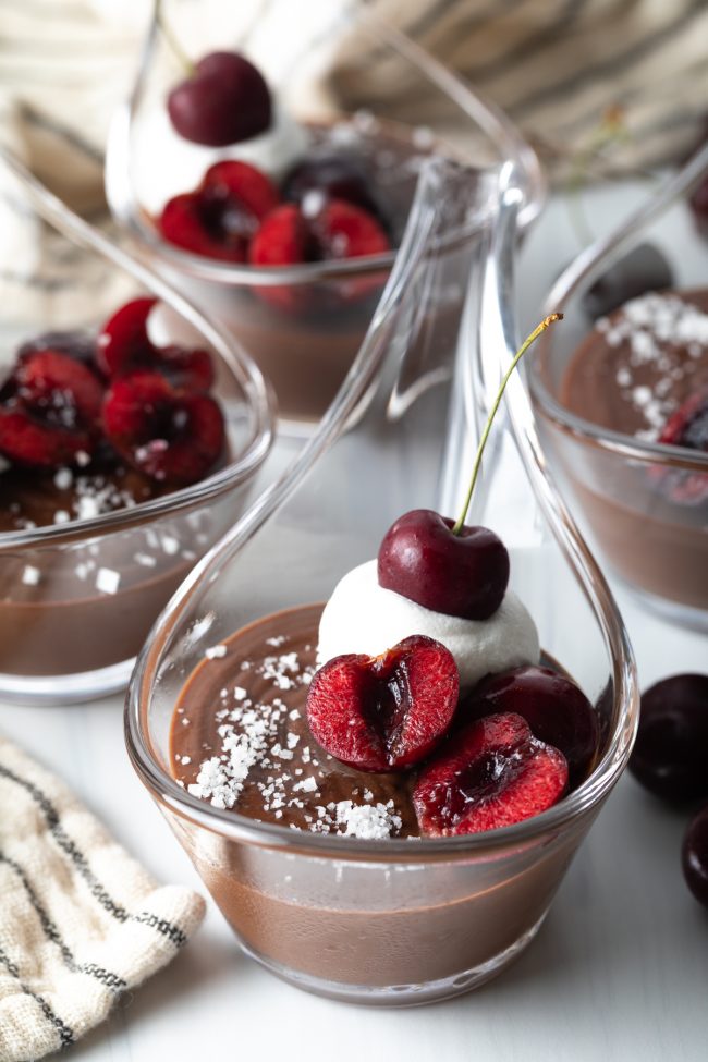close view of serving of Italian chocolate pudding with cherry halves, whipped cream, and sea salt