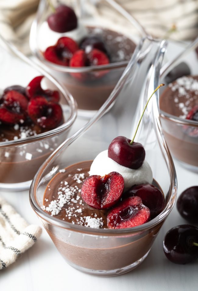 close view servings of chocolate budino in with whipped cream and cherries