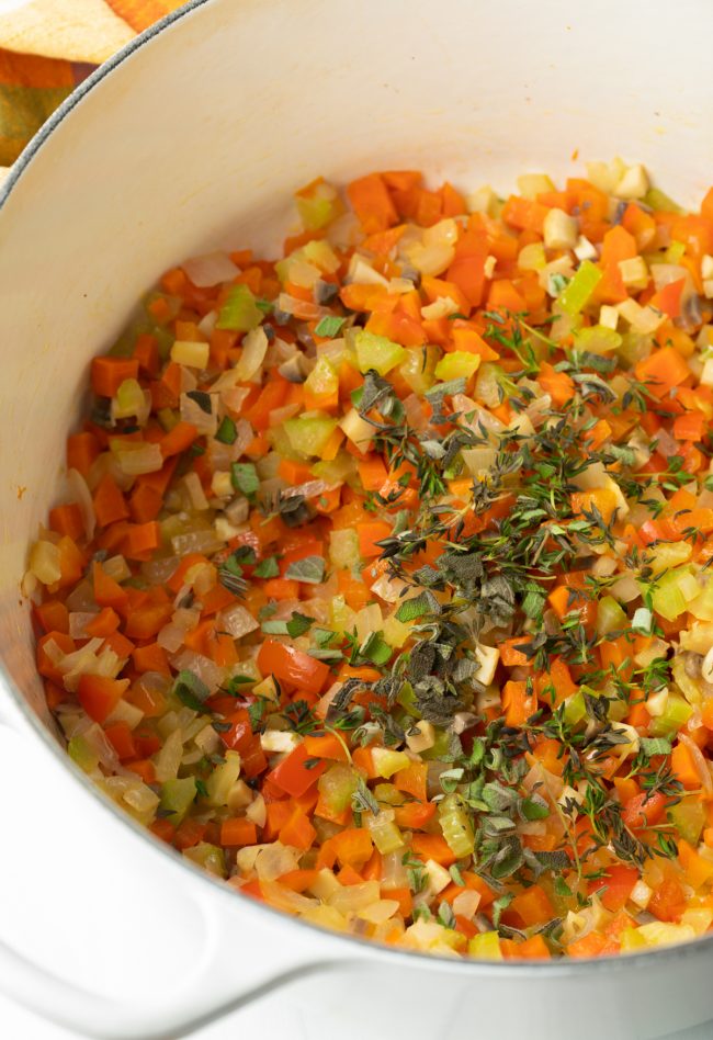 white pot with sauteed chopped carrots, celery, onion, and fresh herbs