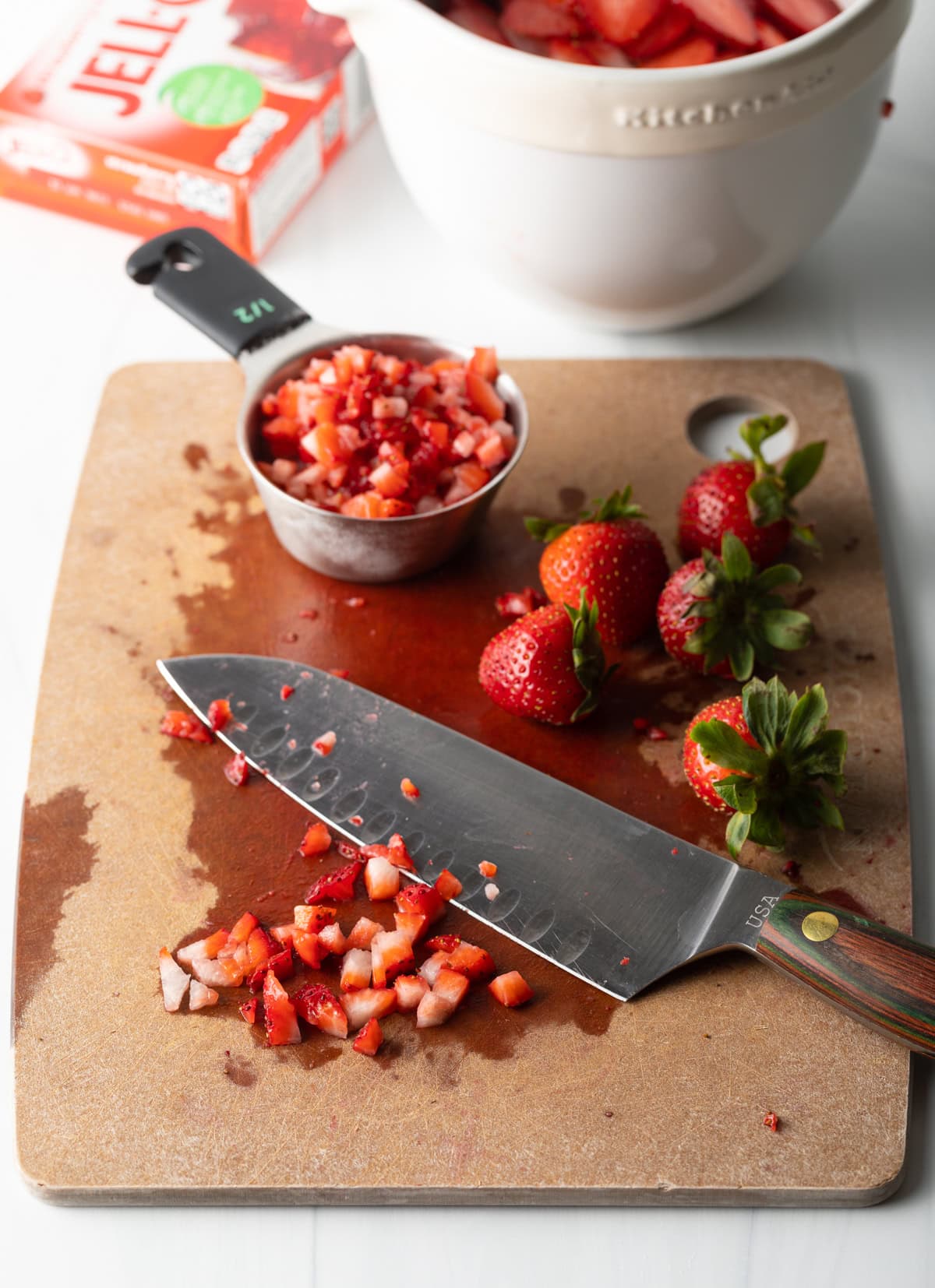 Cutting board with large knife, whole and diced strawberries on the board.