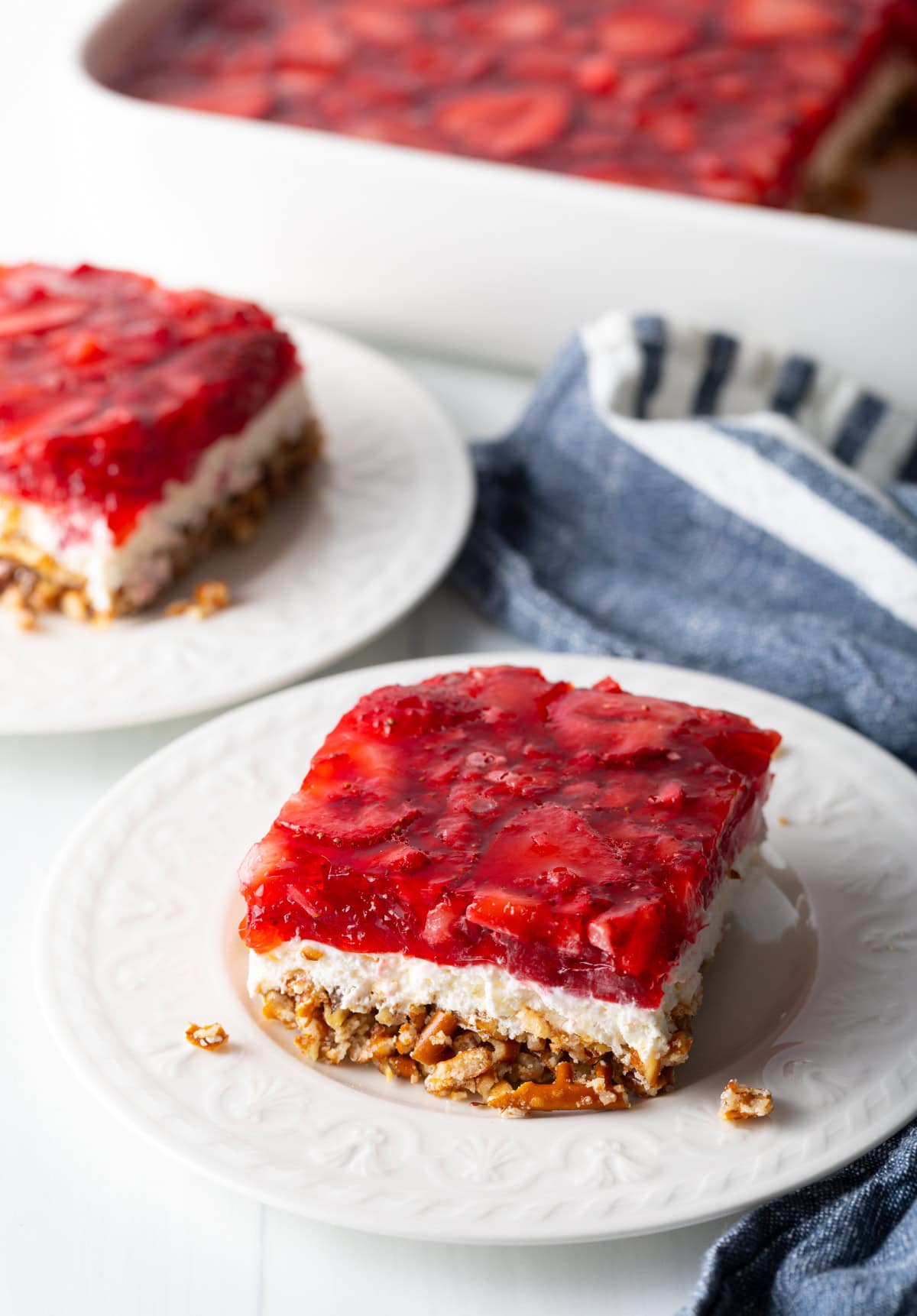 Side view of square piece of strawberry pretzel salad recipe on a white plate.