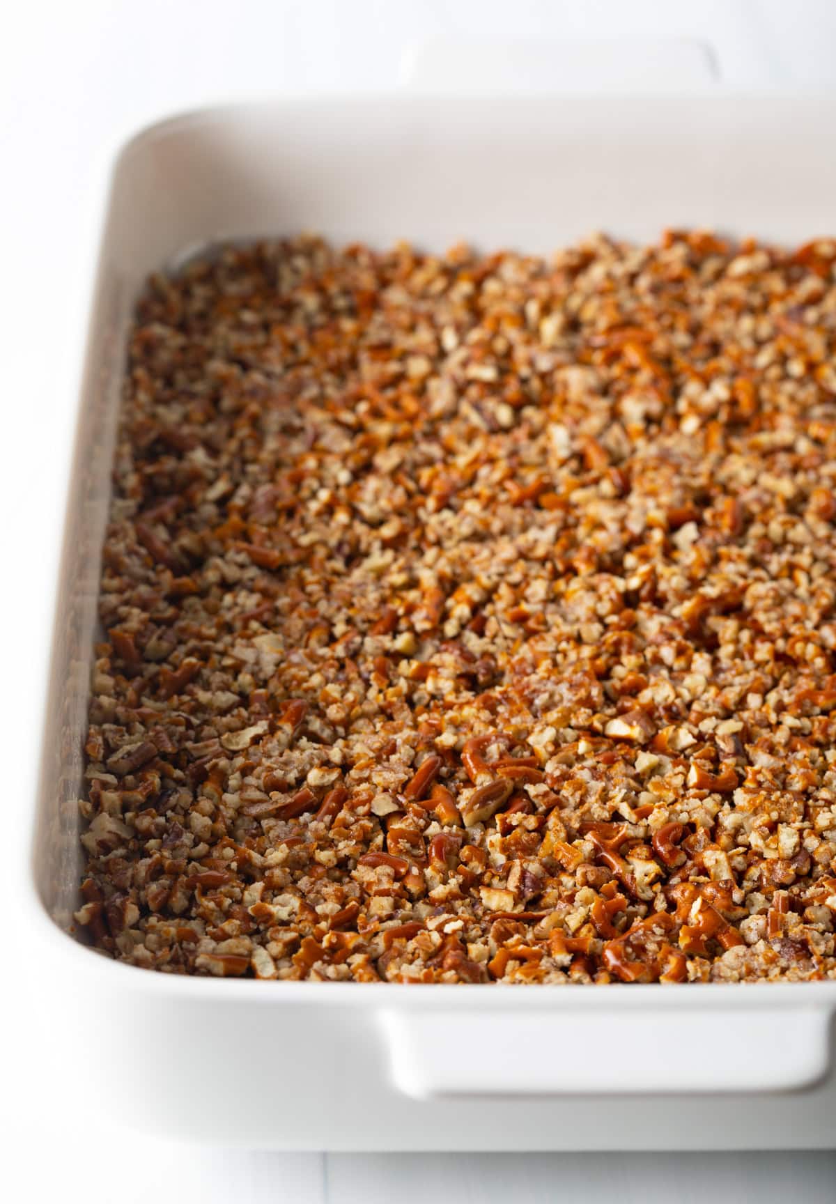 Layer of tightly packed pretzels and pecans in the bottom of a white baking dish.