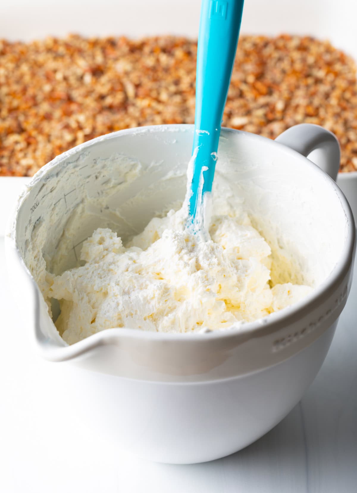 Bowl with cream cheese and cool whip fluff, being stirred by a blue spatula.