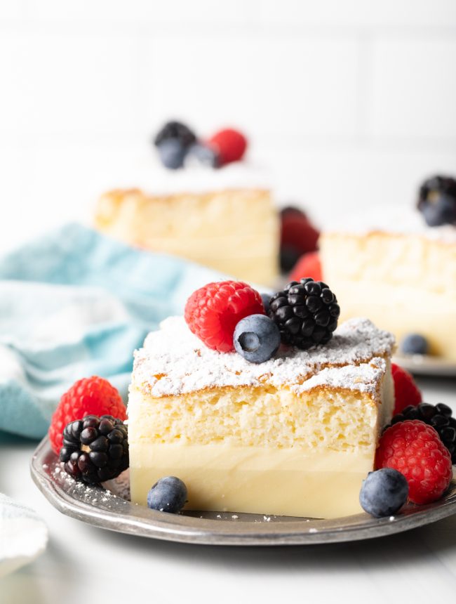 close side view of magic cake with 3 distinct custard layers, on a plate with fresh berries