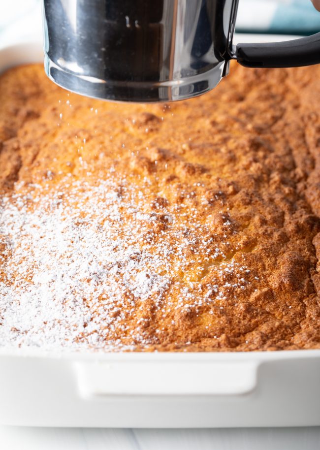 sifting the top of the golden brown baked cake with powdered sugar