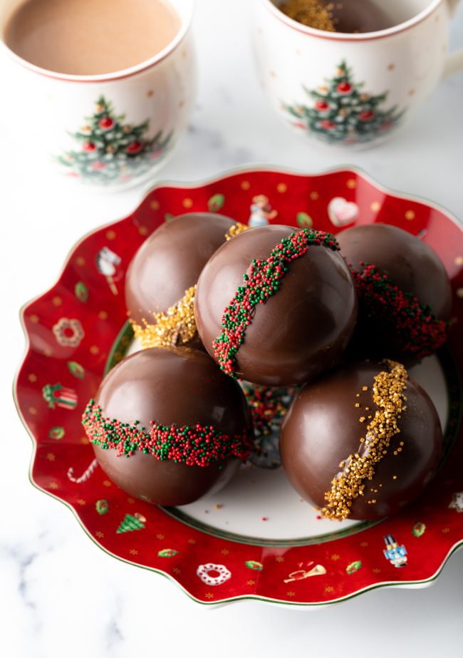 top down view five festive hot cocoa bombs with marshmallows inside on a christmas plate