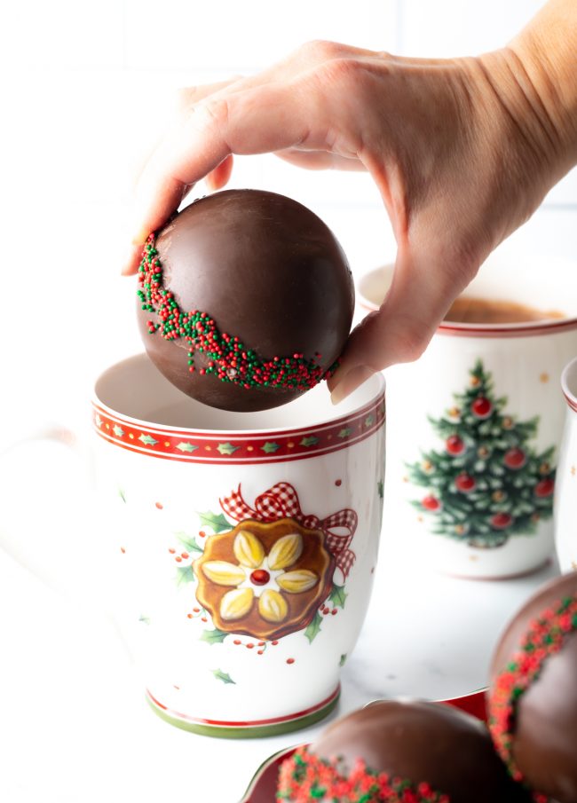 hand holding hot chocolate ball over a christmas mug