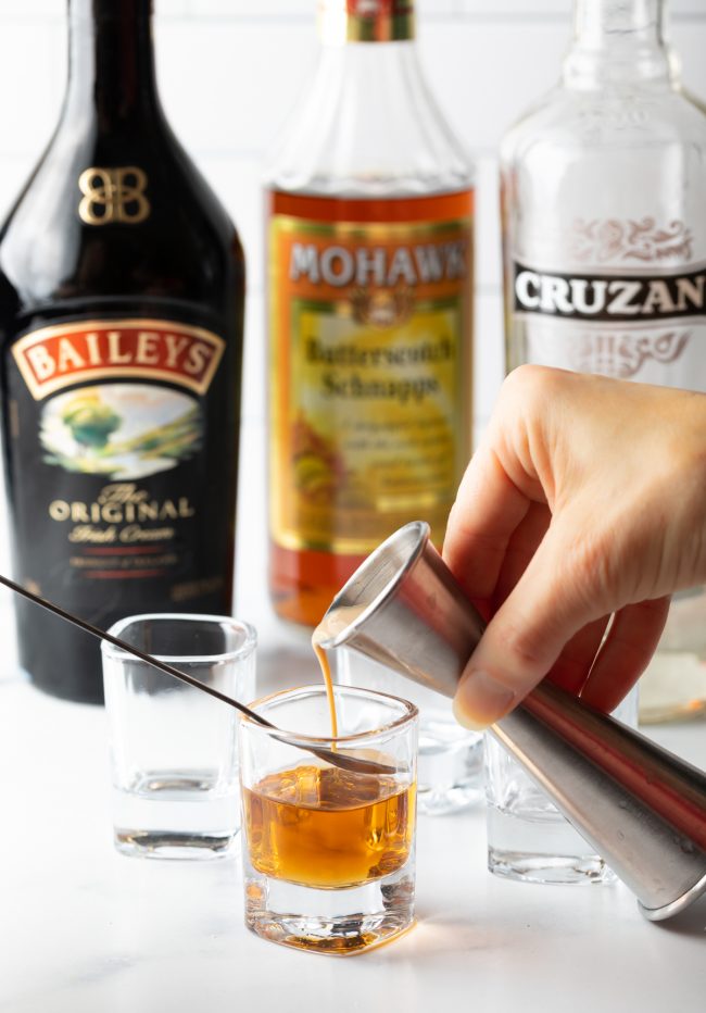 adding irish cream to the butterscotch schnapps in a shot glass