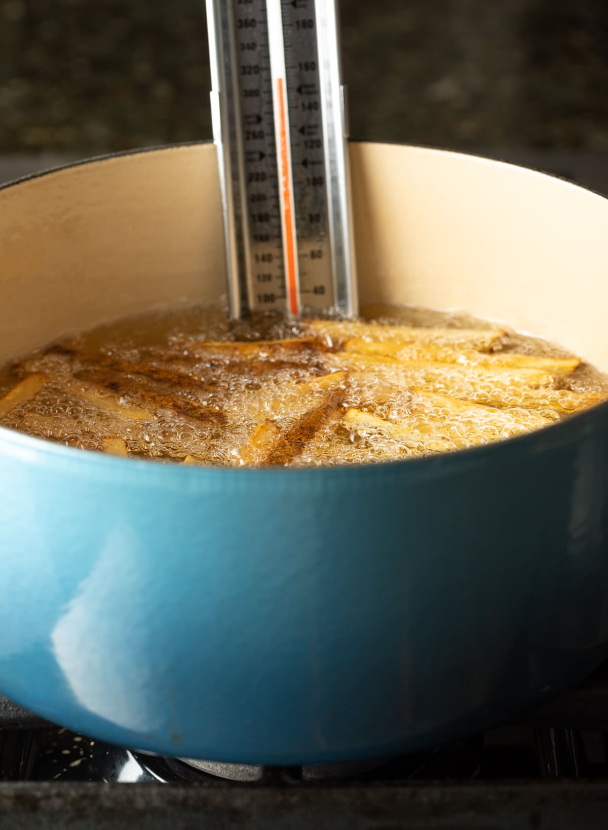 Thermometer clipped to dutch oven filled with hot oil while frying potatoes.