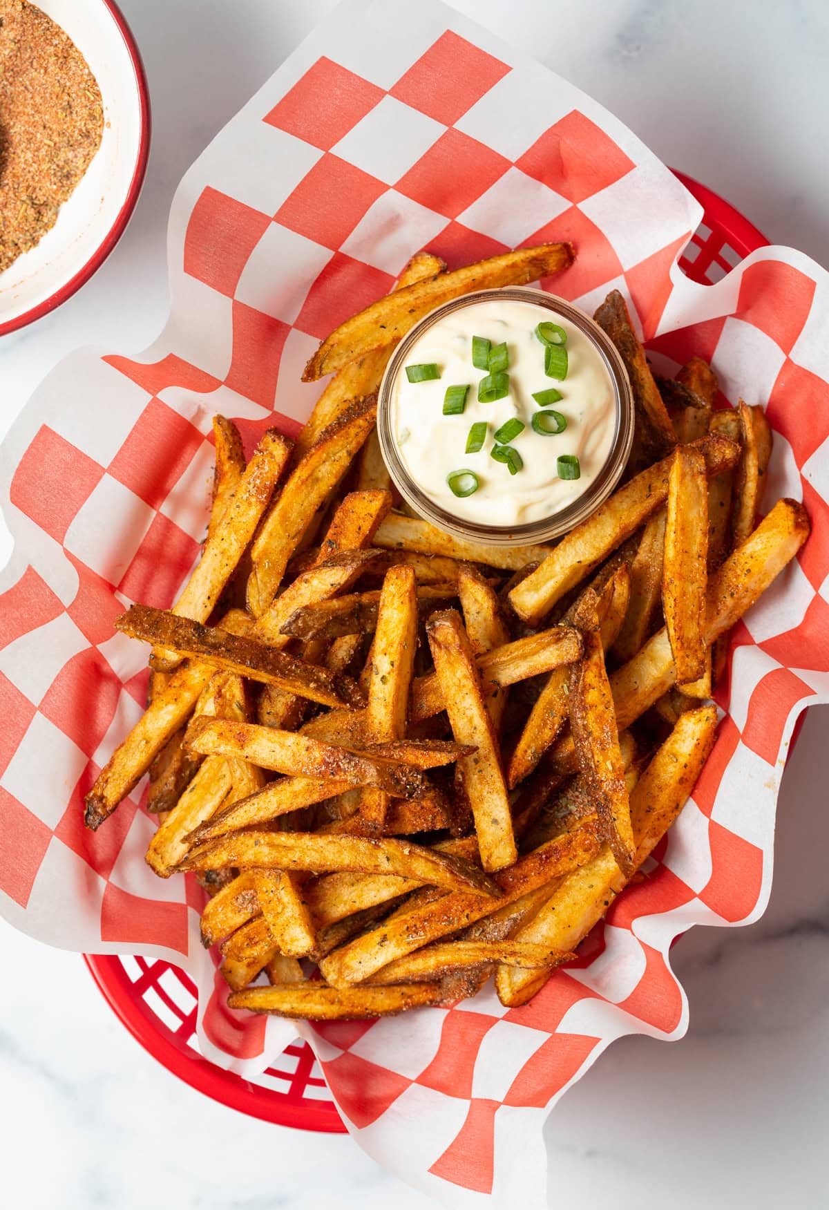 Top view spicy Cajun fries in a basket with sauce in a small cup of sauce.