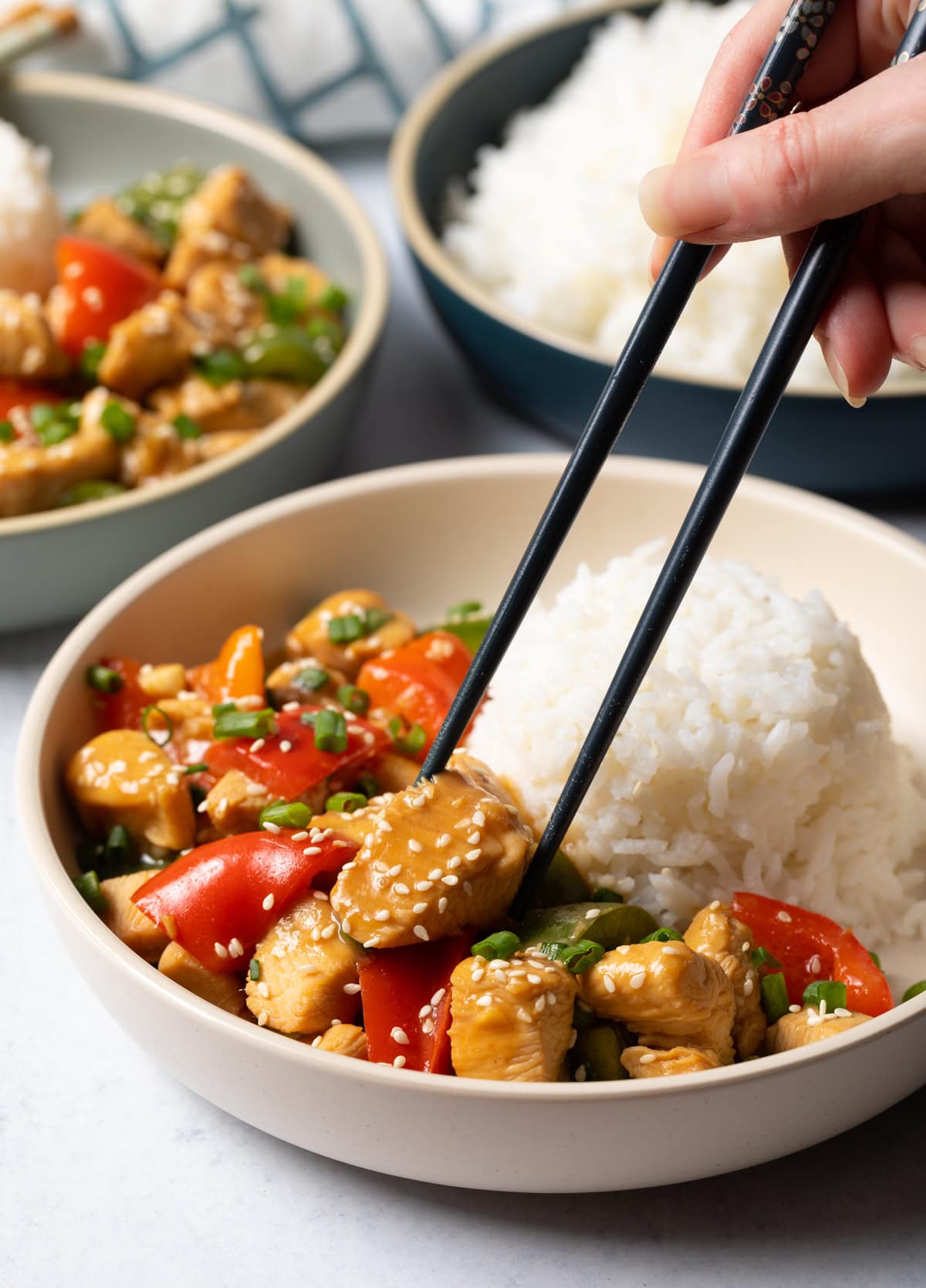 Hand with chopsticks grabbing piece of chicken from the bowl.
