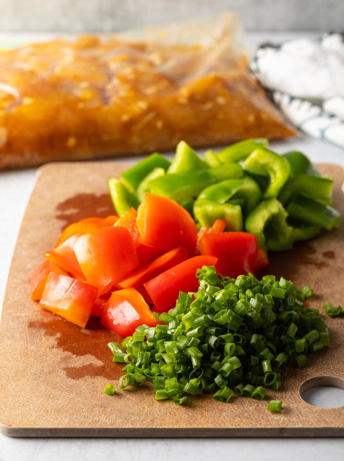 Cutting board with chopped red and green bell peppers, plus sliced scallions.