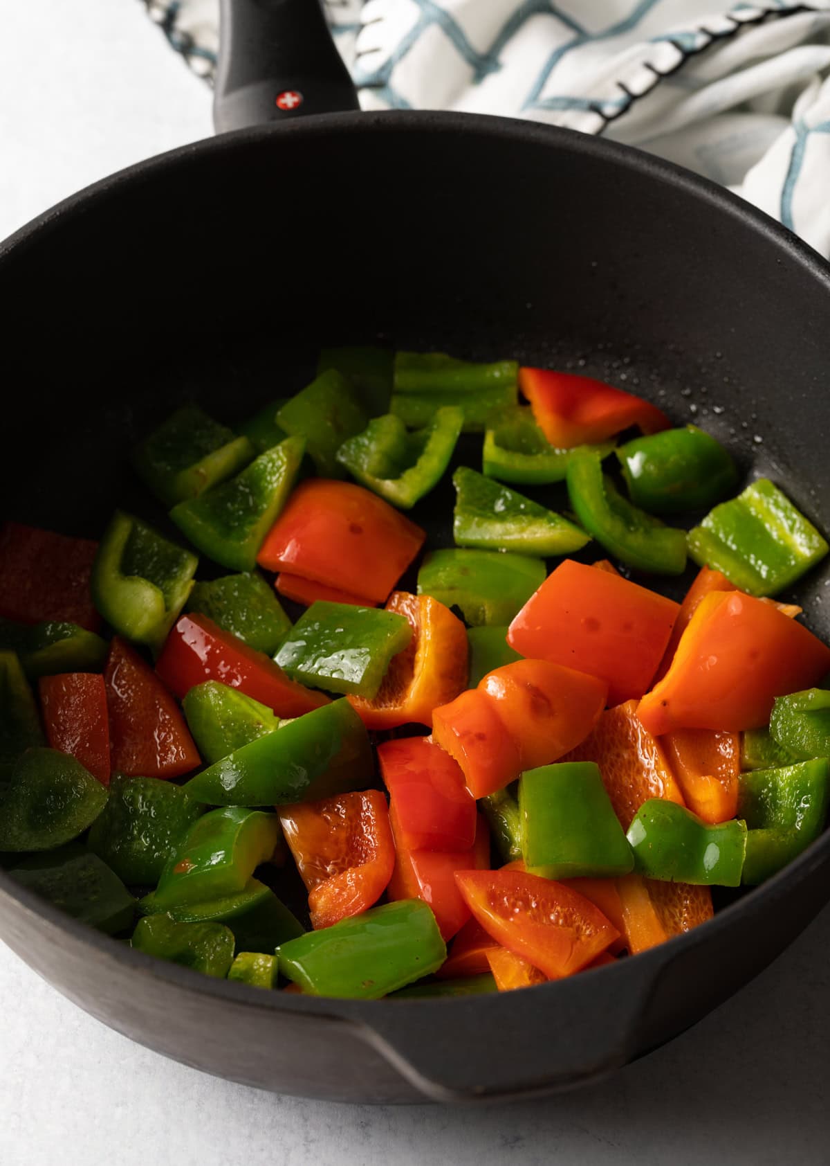Large black skillet with chopped red and green bell peppers.