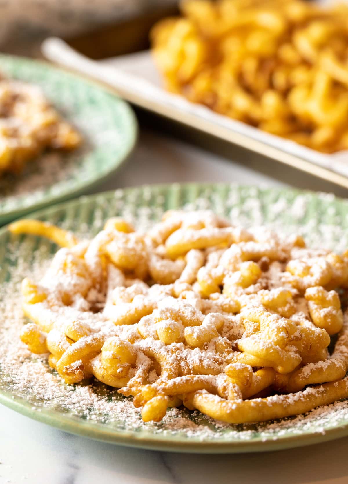 A homemade funnel cake recipe topped with powdered sugar, sitting on a green plate.