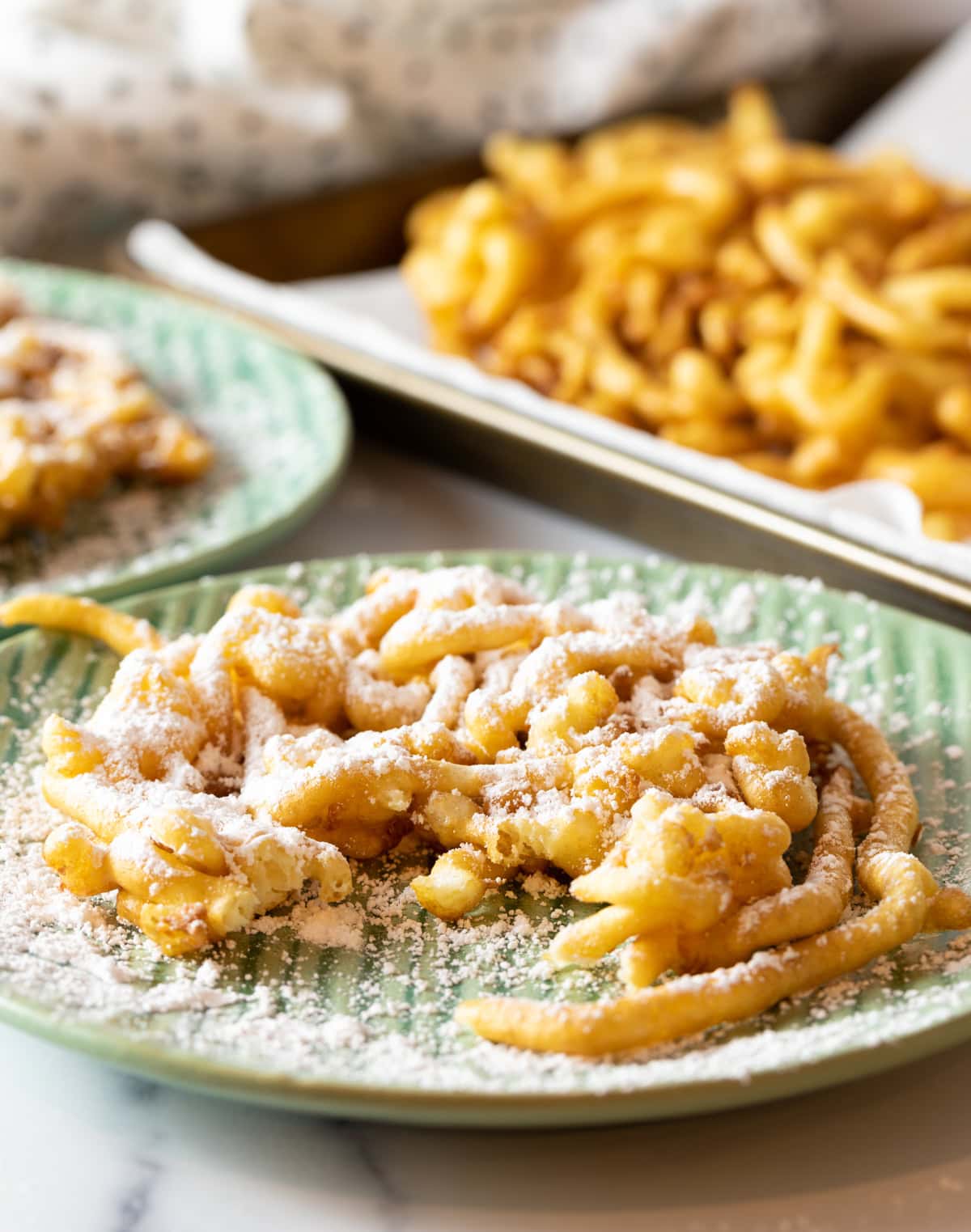 Fresh homemade funnel cake topped with powdered sugar, sitting on a green plate with a piece taken out.