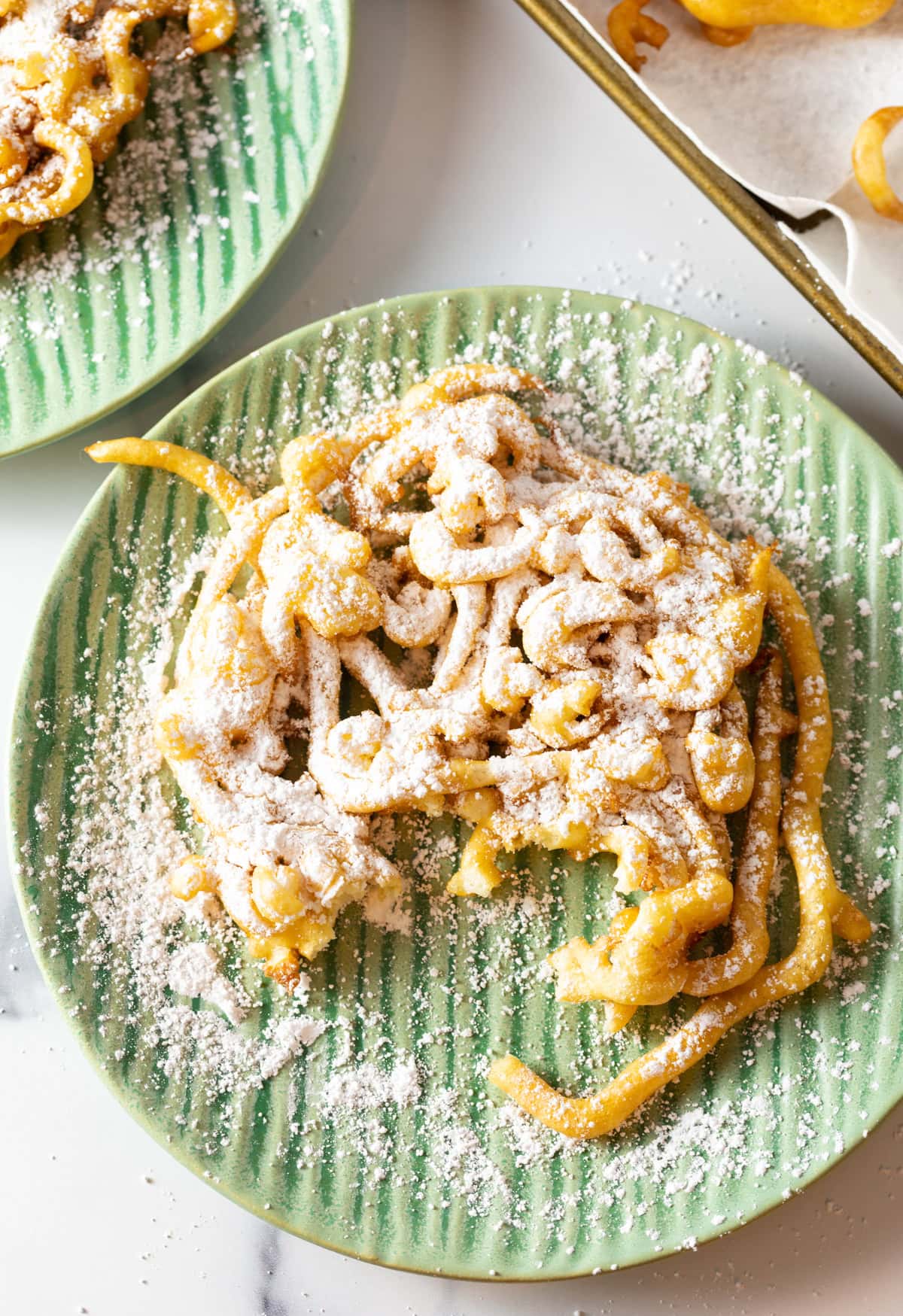 An easy homemade funnel cake recipe topped with powdered sugar, sitting on a green plate with a piece taken out.