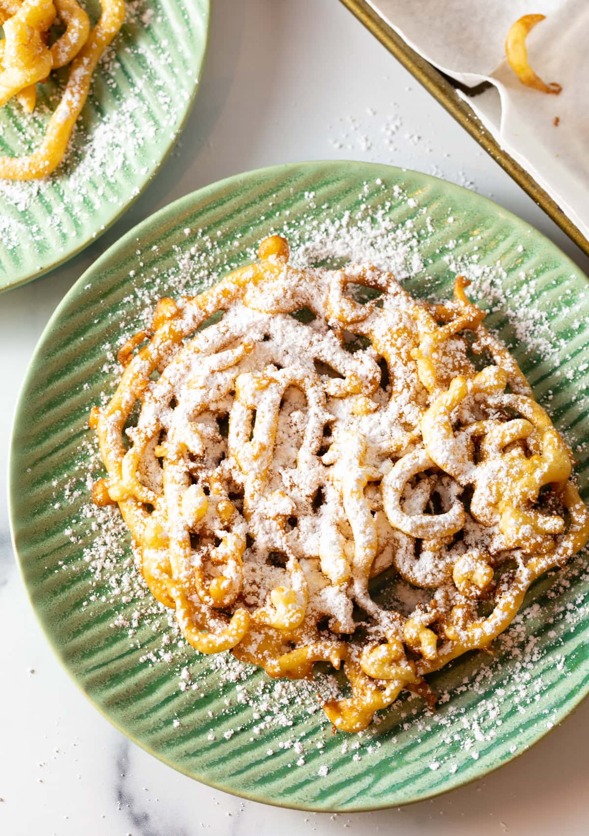 Overhead shot of homemade funnel cake on a green plate.