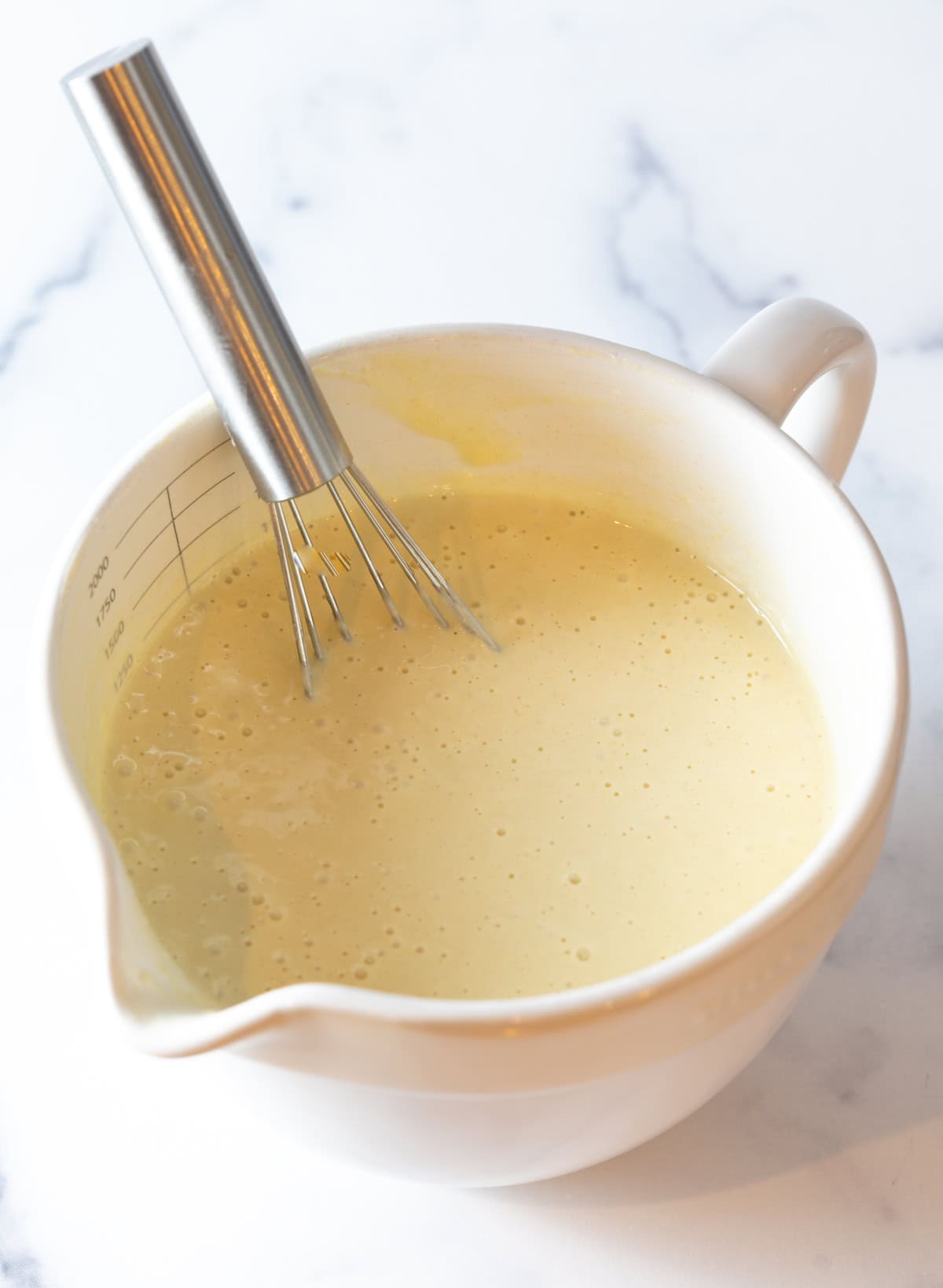 Homemade funnel cake batter being whisked in a white mixing bowl.