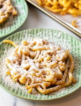 Overhead shot of homemade funnel cake with powdered sugar on a green plate.