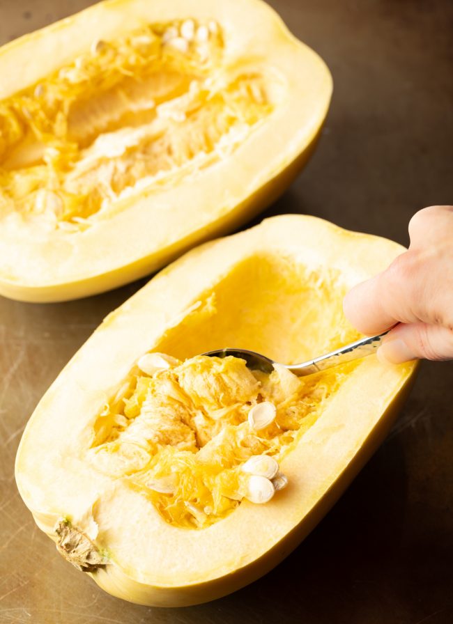 raw squash halve with spoon scooping out the seeds