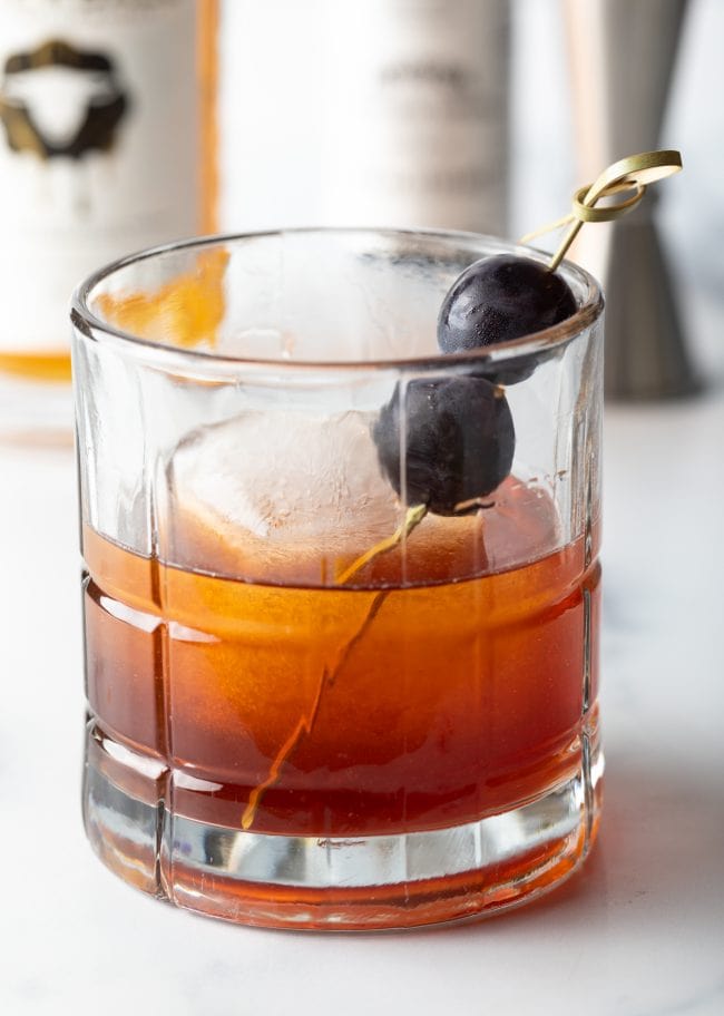 Skrewball peanut butter whiskey and jelly syrup drink in a glass with ice and grape garnish.