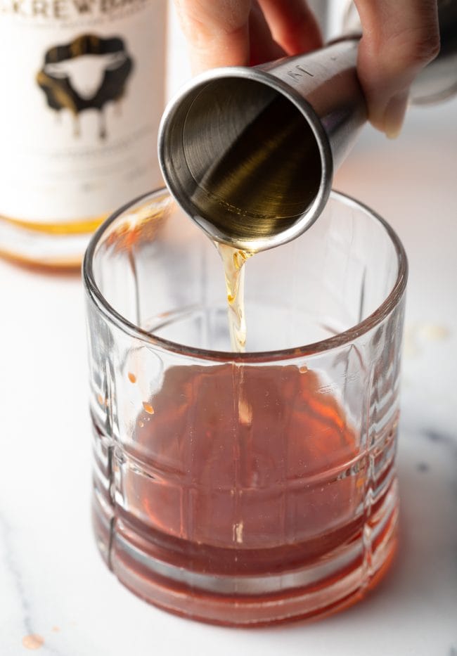 Closeup shot of hand pouring alcohol into a lowball glass. 