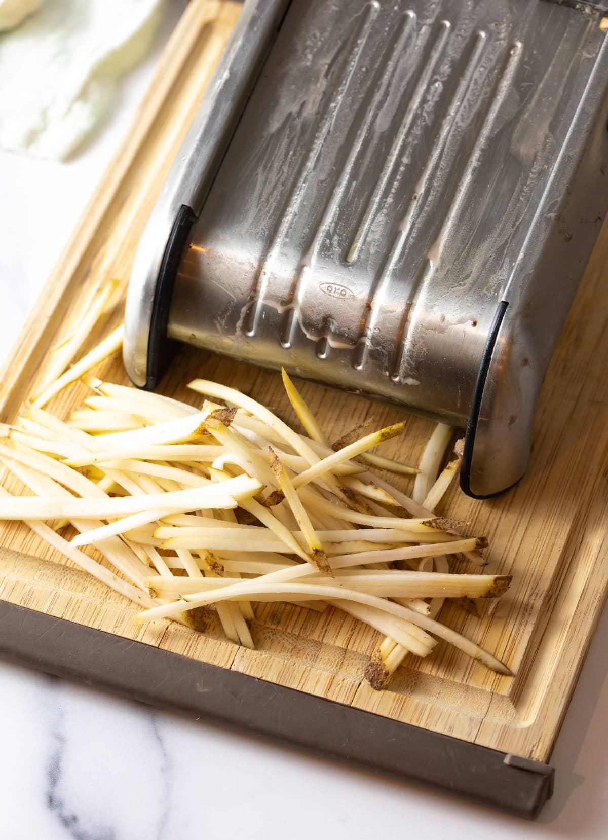 Mandolin slicer on a wood cutting board with raw thin slices of potatoes.