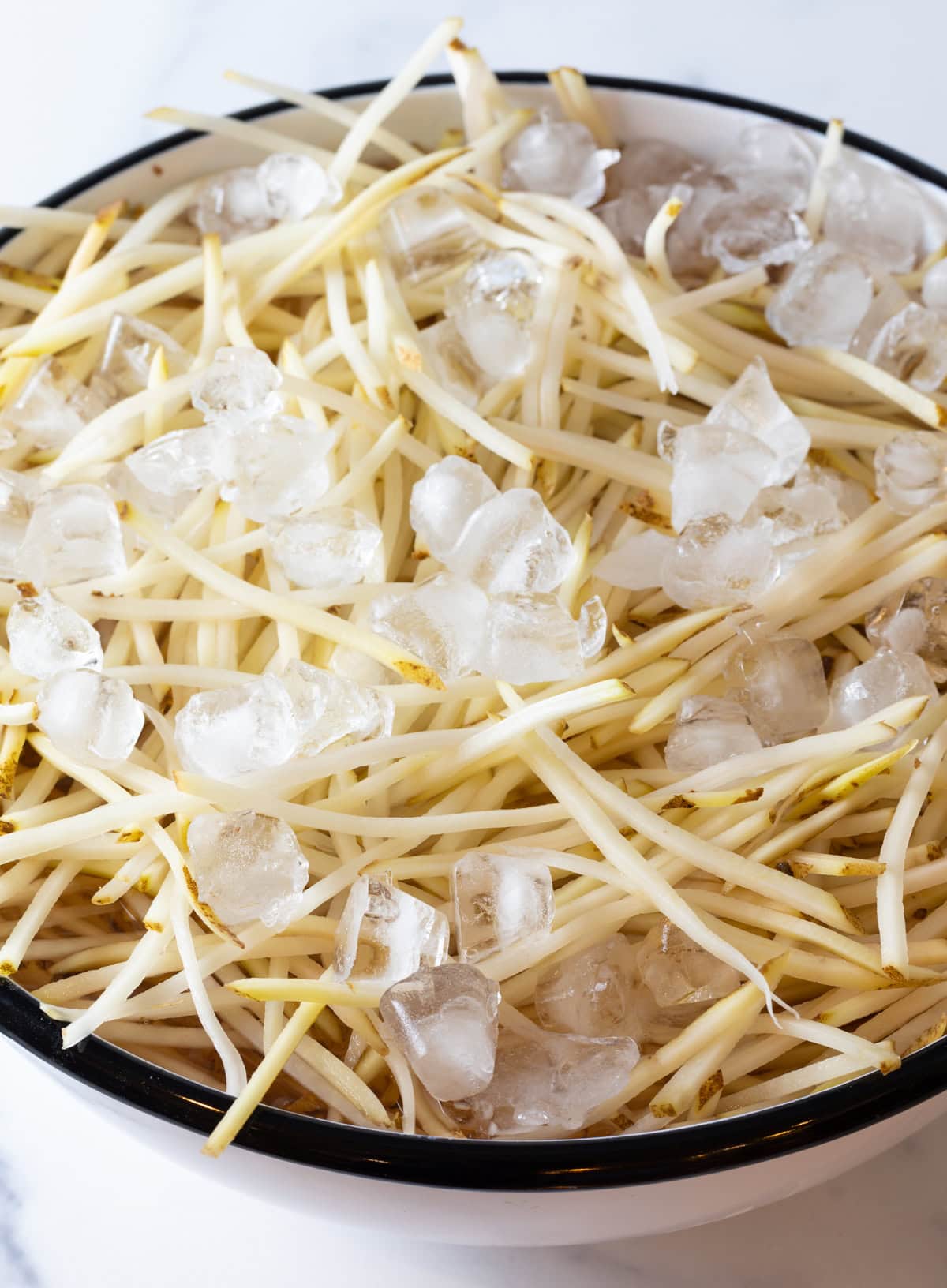 Bowl of ice water with raw slices of potatoes.