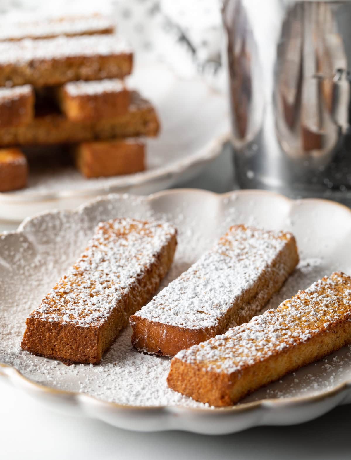 Three French toast sticks made in the air fryer sitting on a white plate, topped with powdered sugar.