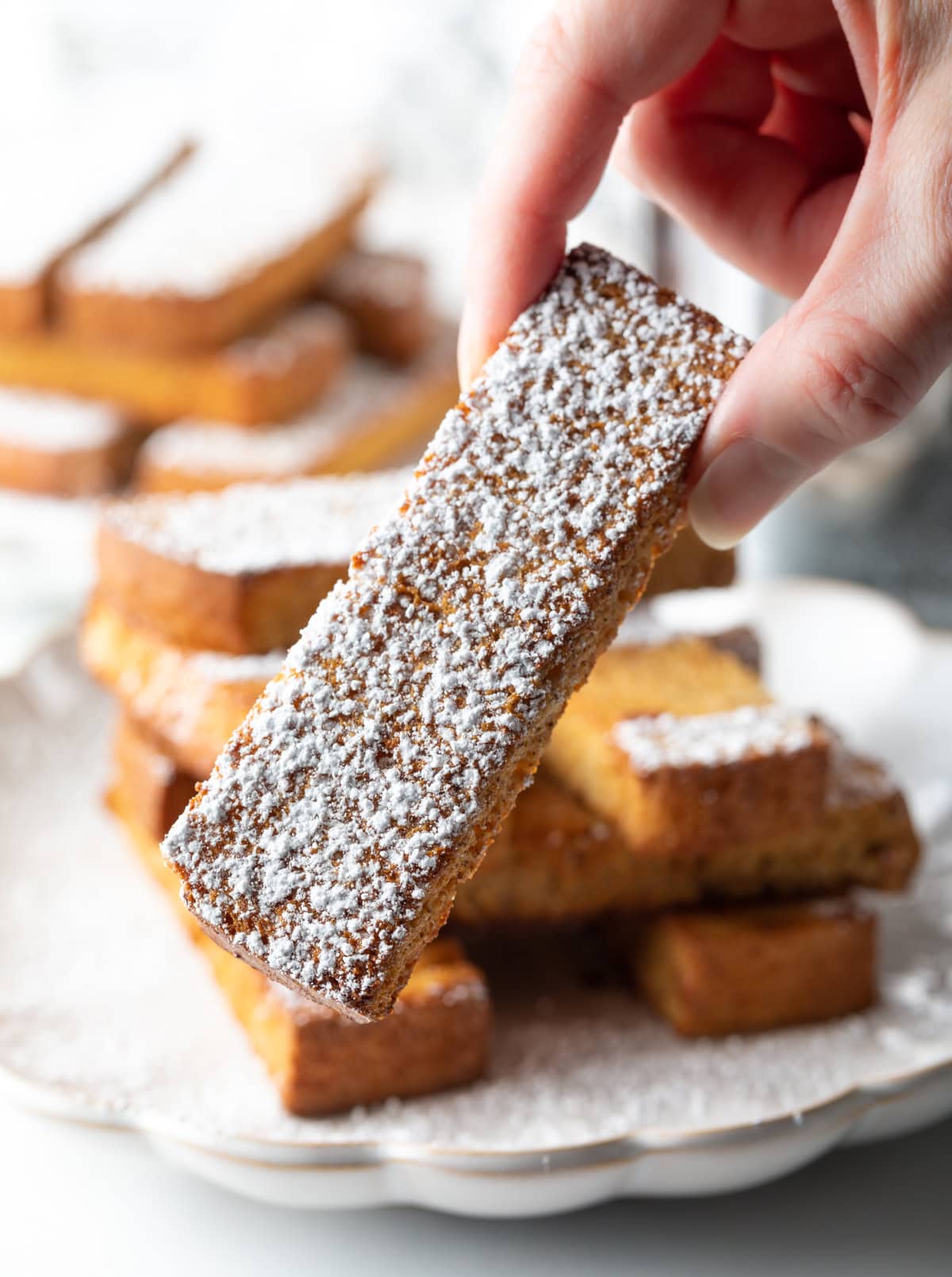 A hand is holding an air fryer French toast stick covered in powdered sugar.