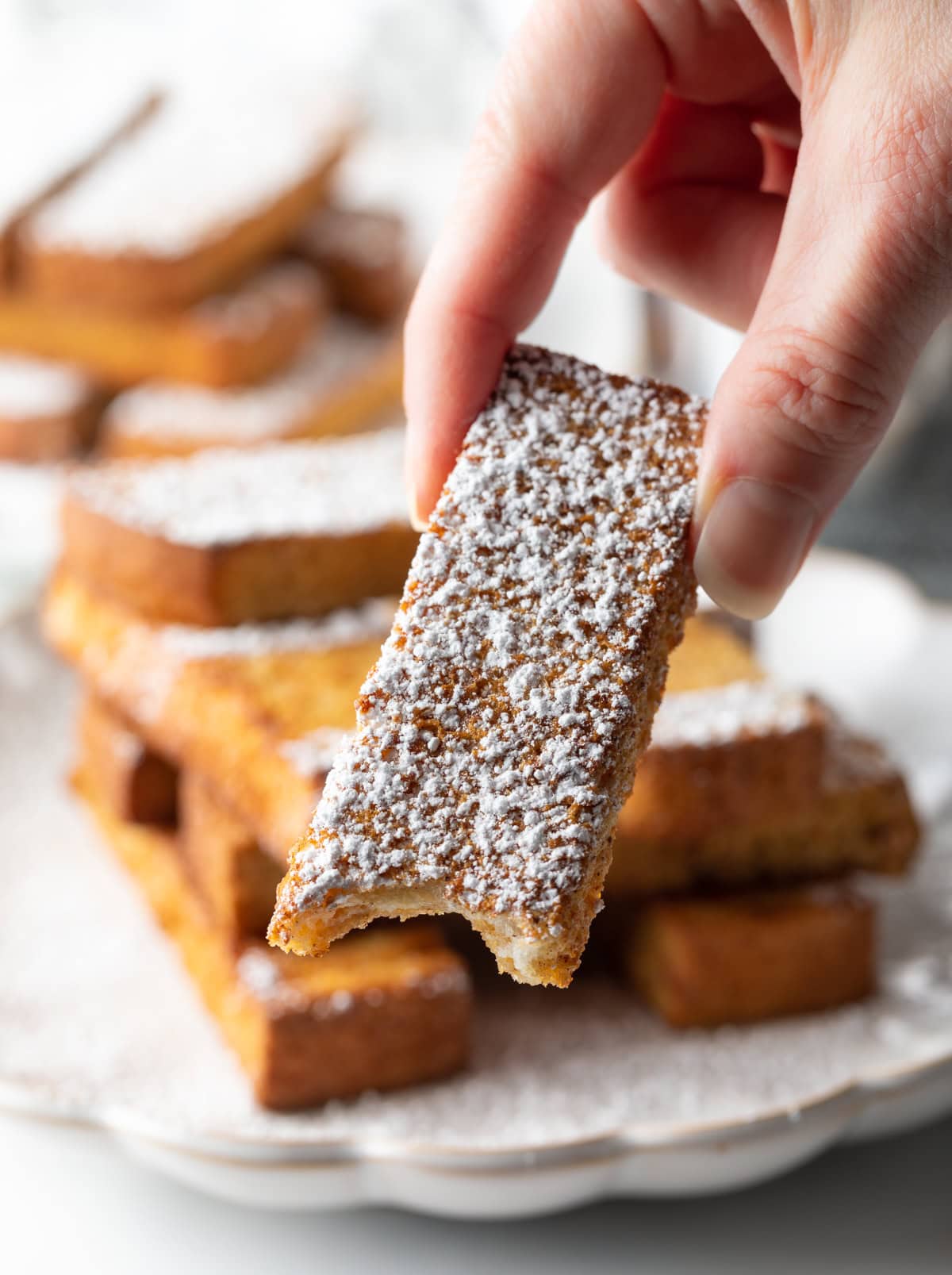 A hand is holding an air fryer French toast stick with a bite taken out.