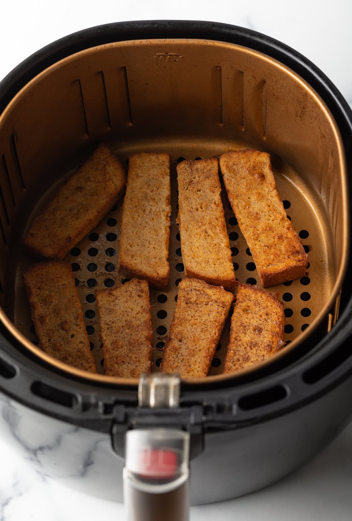 An air fryer basket filled with French toast sticks made in the air fryer.