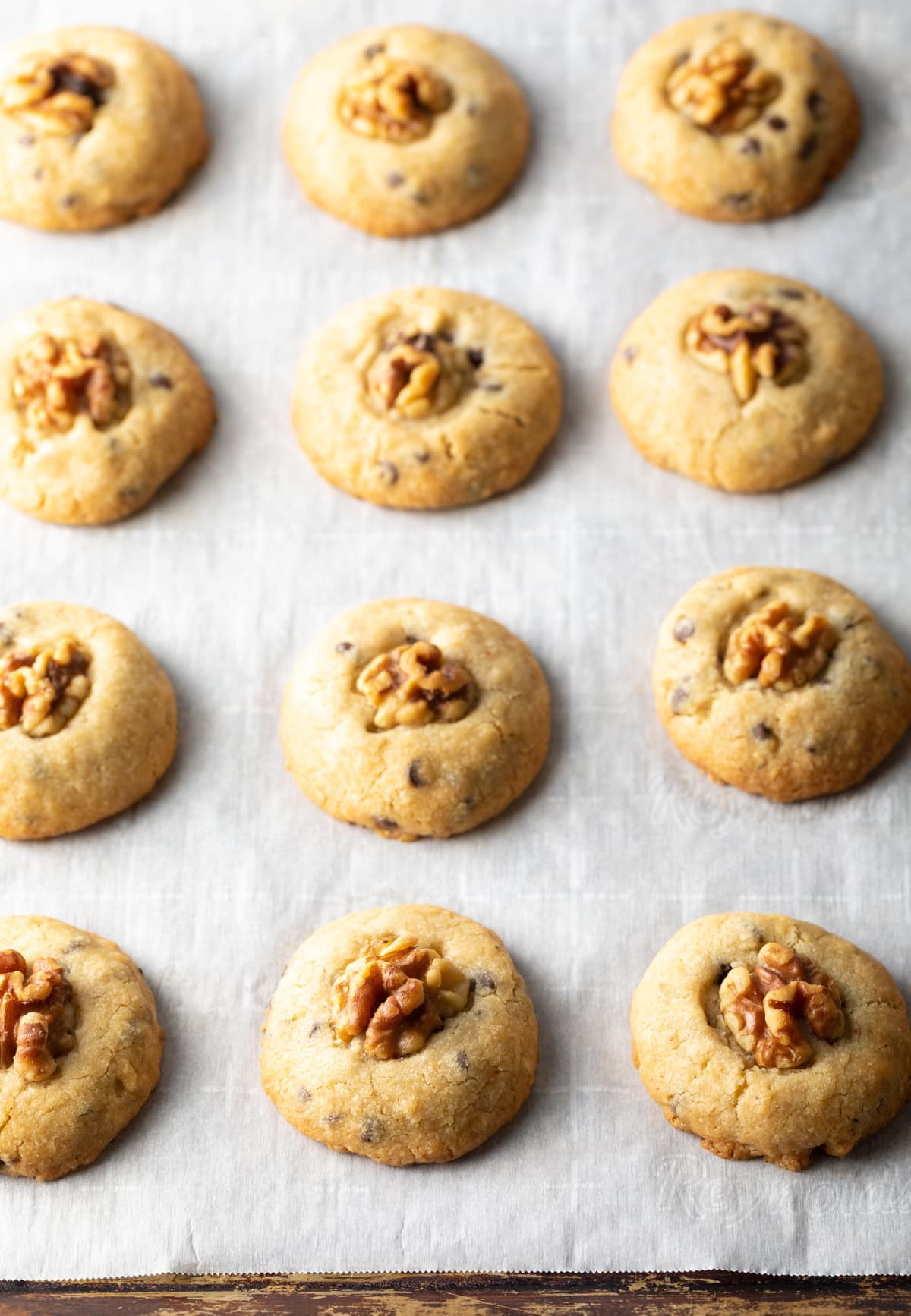 Chocolate chip and walnut cookies lined up on a baking tray with white parchment paper.