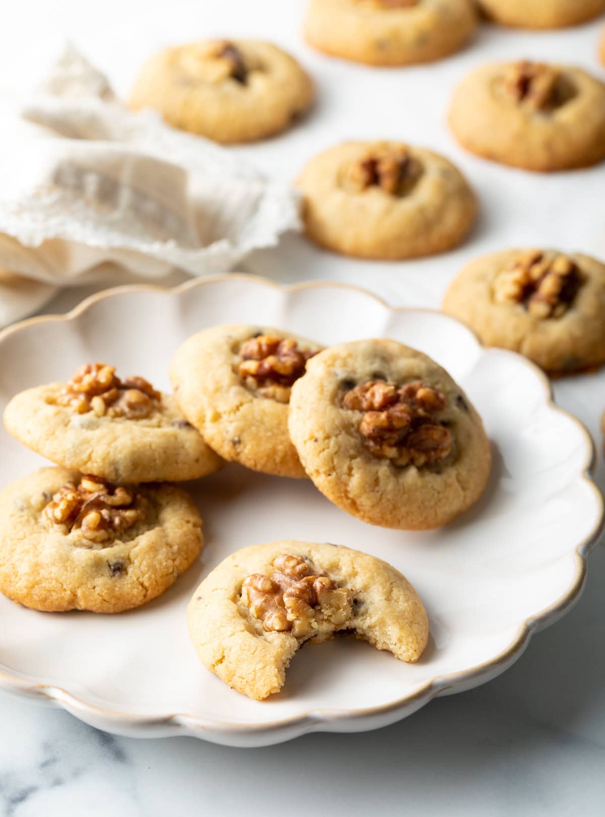 Chocolate chip walnut cookies stacked in a semi-circle on a white plate, with one cookie that has a bite taken out of it.