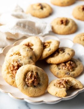 Chocolate chip walnut cookies lined up in a circle on a white plate, one cookie has a bite taken out of it.