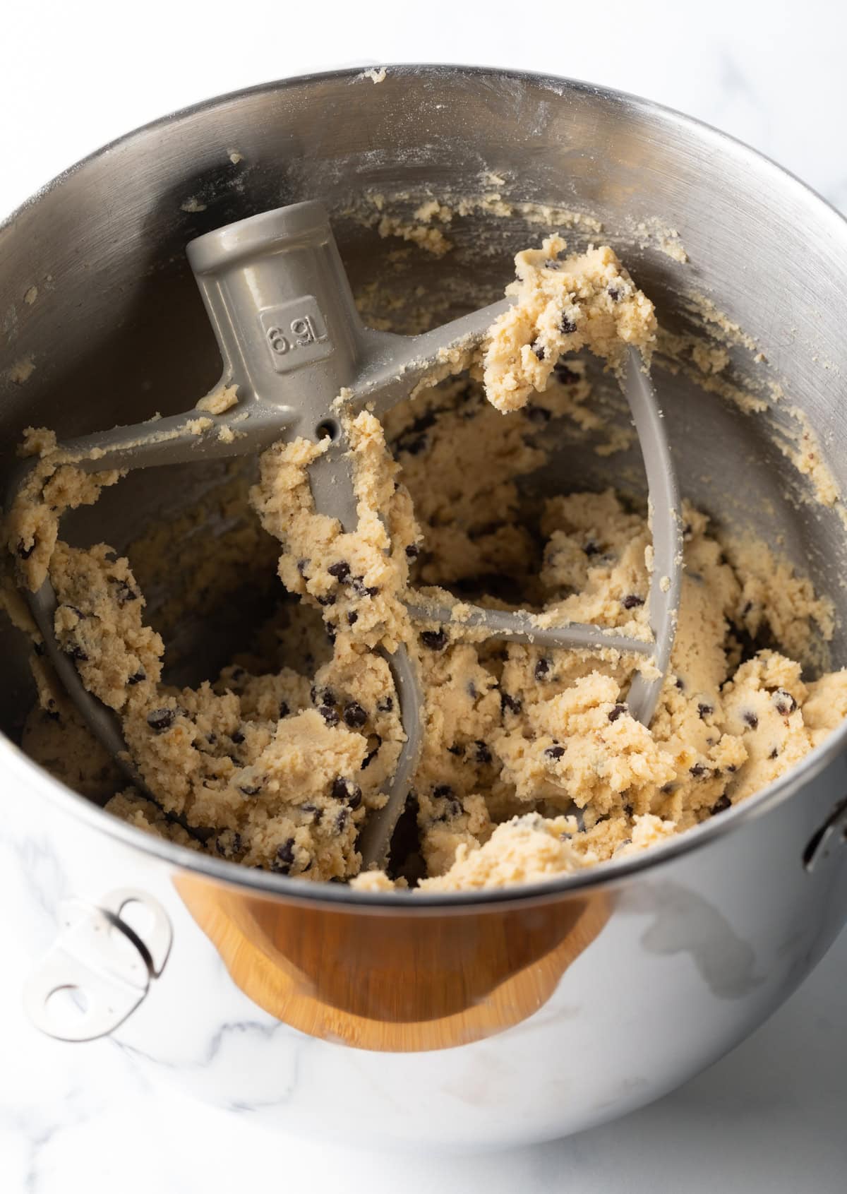 A stand mixer is mixing a butter, sugar, walnut, and chocolate chip mixture for a chocolate chip walnut cookies recipe.