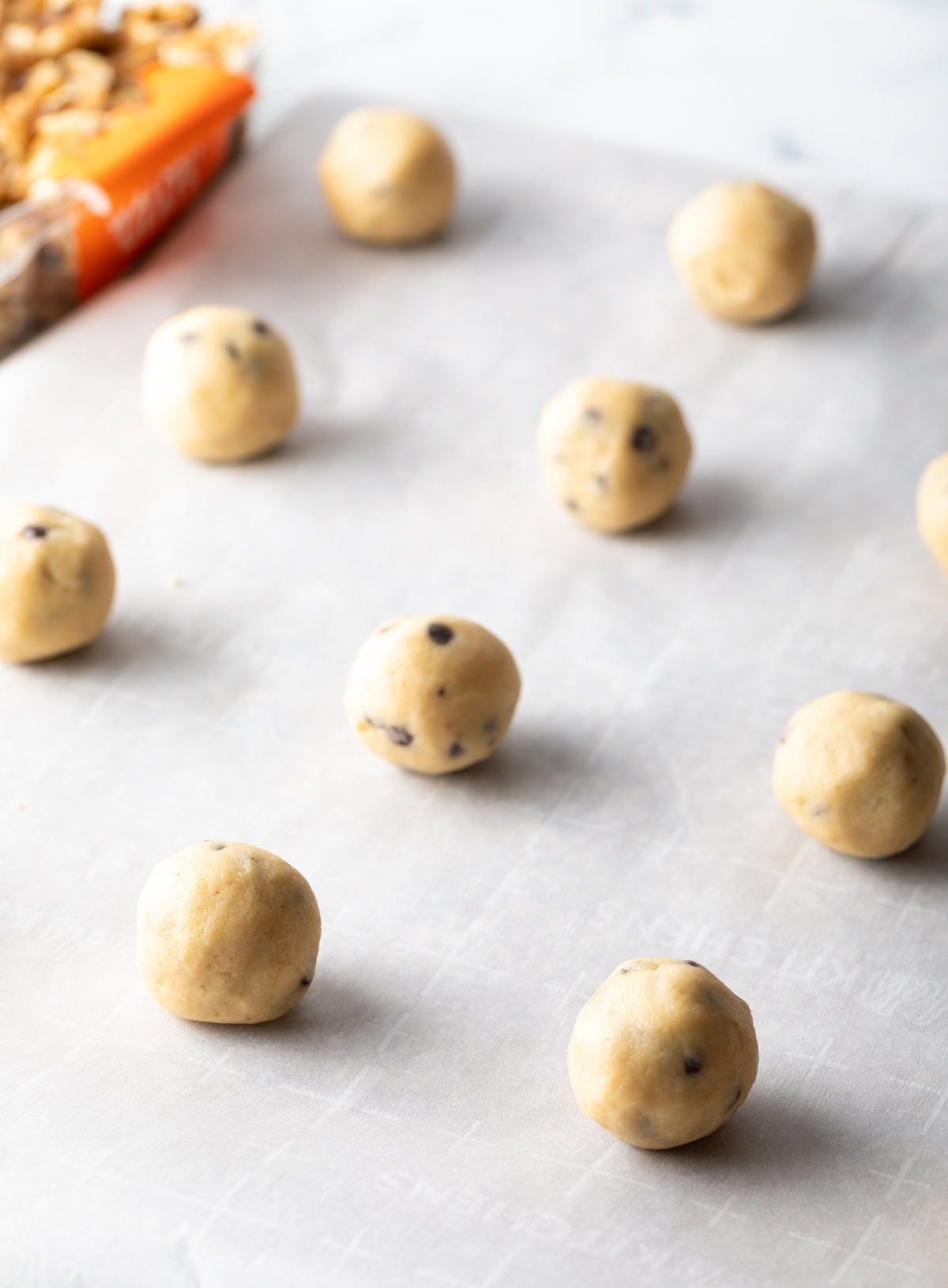 Chocolate chip walnut cookie dough formed into balls and lined up on a baking sheet with white parchment paper.